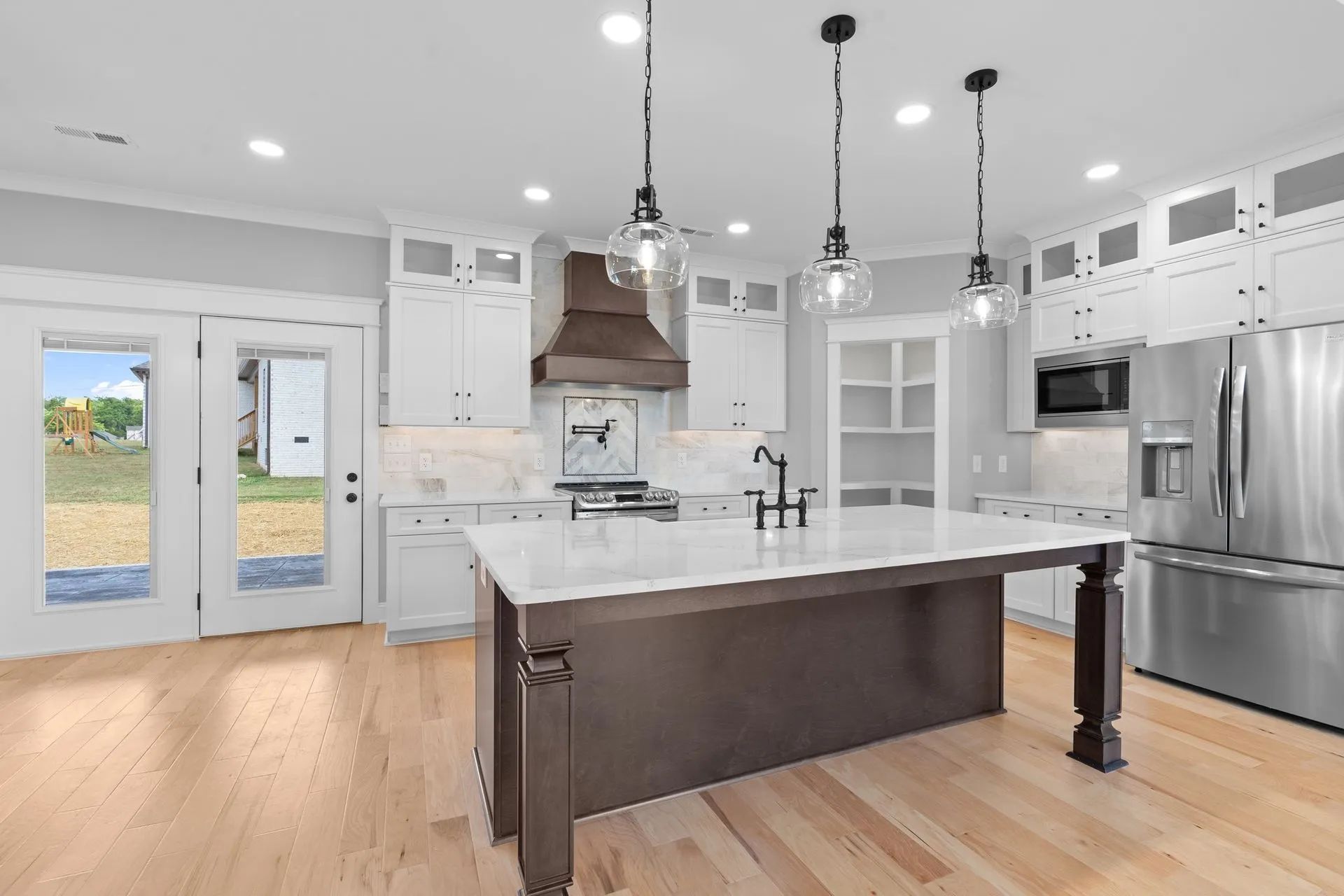 Bright modern kitchen with white cabinets, island, stainless steel appliances, and hardwood floors.