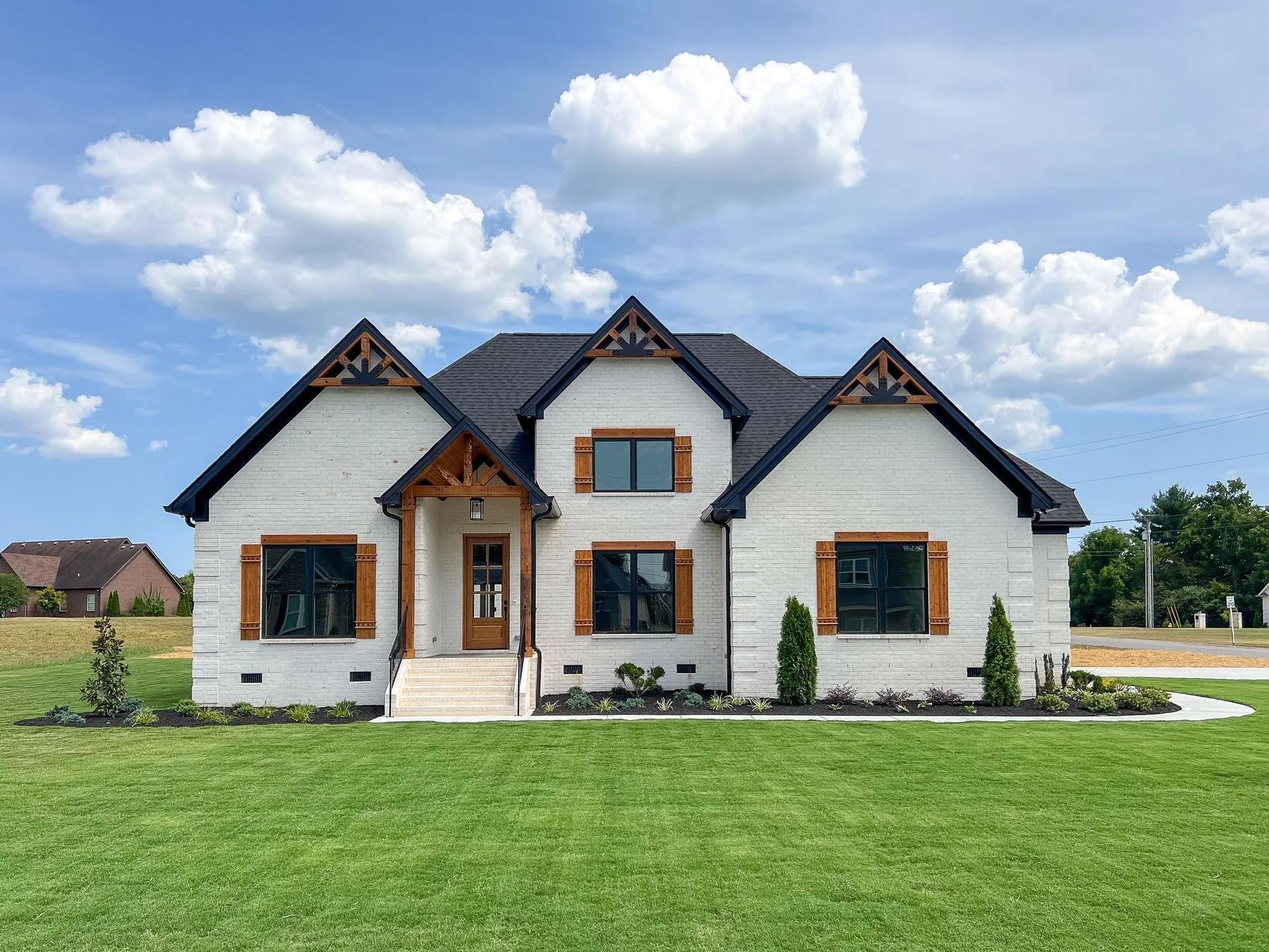 Modern white house with dark roof and brown trim, set on a green lawn under a cloudy blue sky