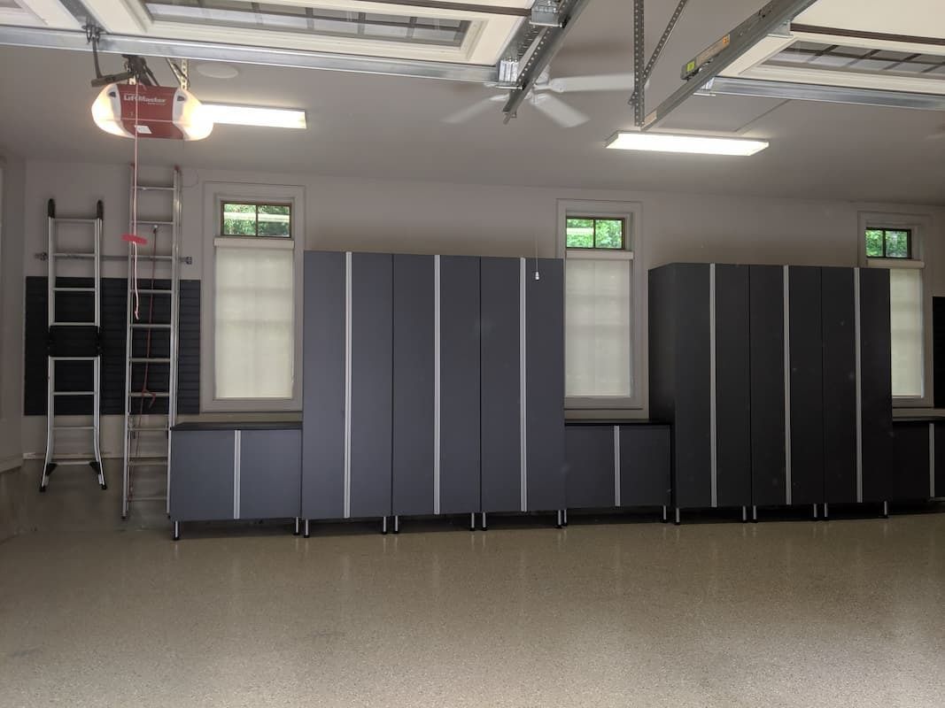 Garage interior with dark gray storage cabinets, windows, and a ladder.