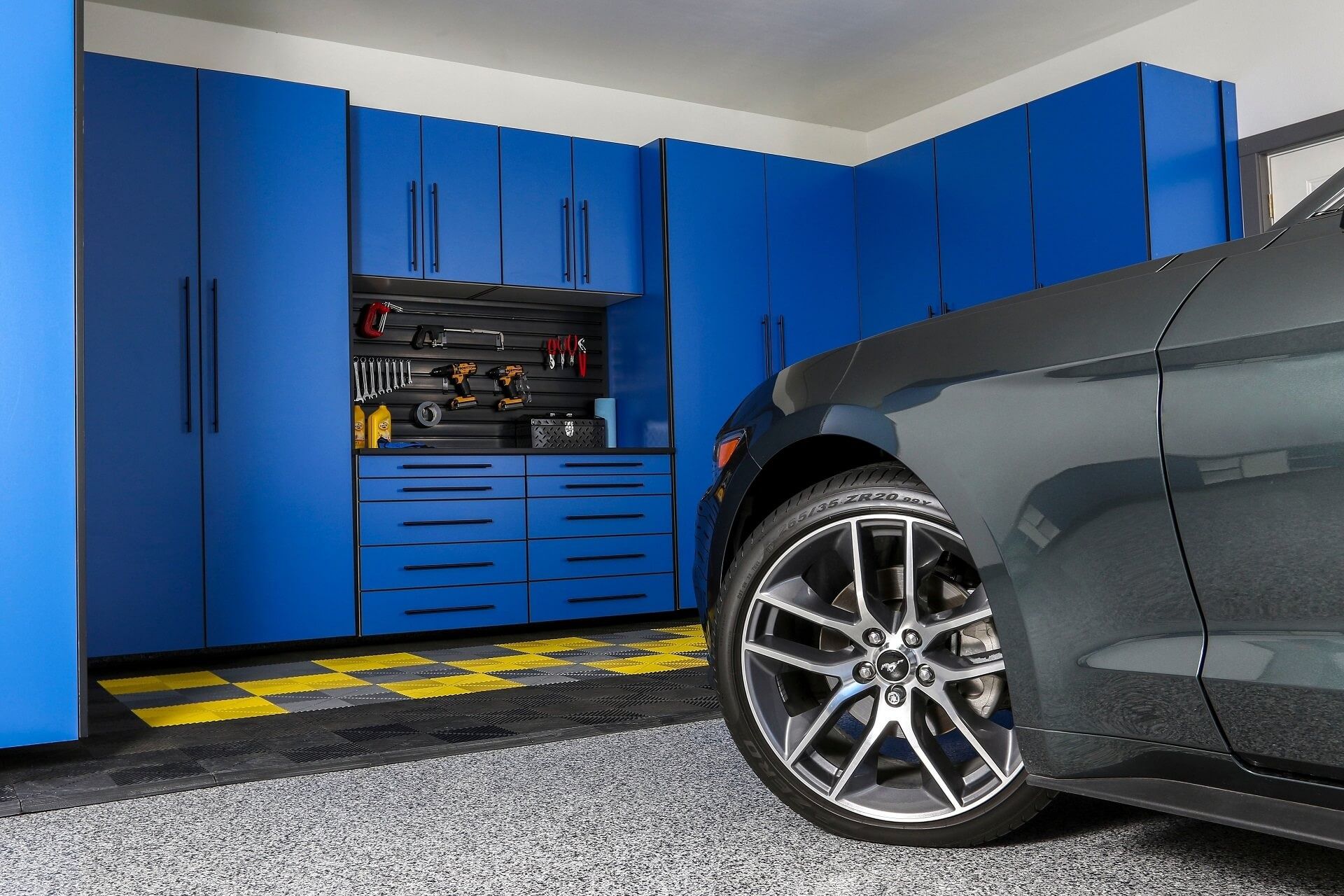 Blue cabinets and tools in a garage with a gray car parked nearby.