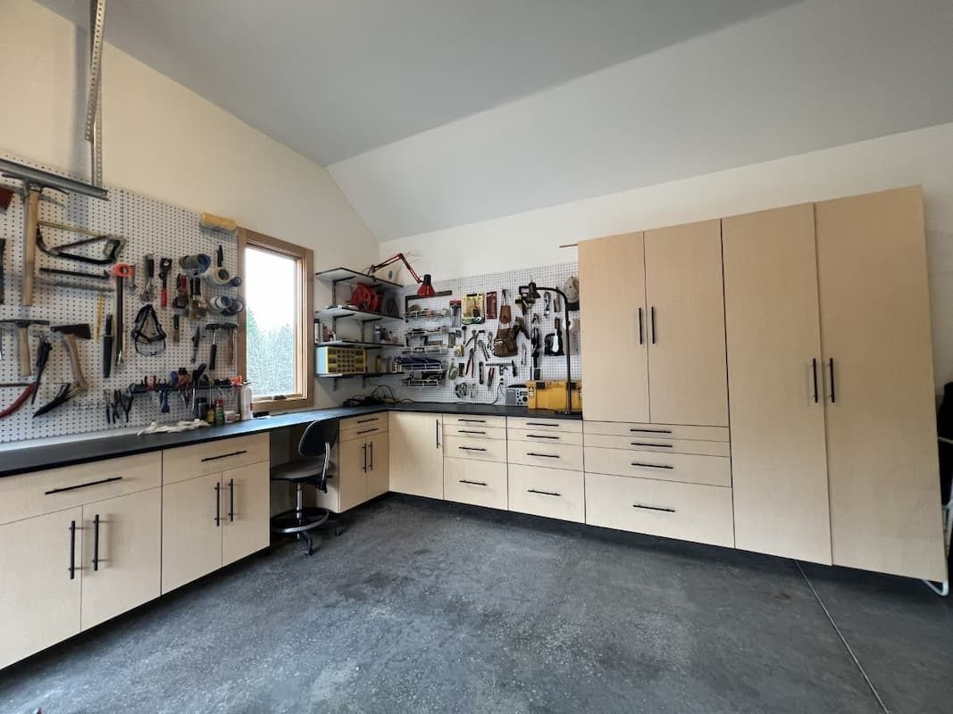 Workshop with light wood cabinets, pegboard tool storage, and a work surface along a wall.