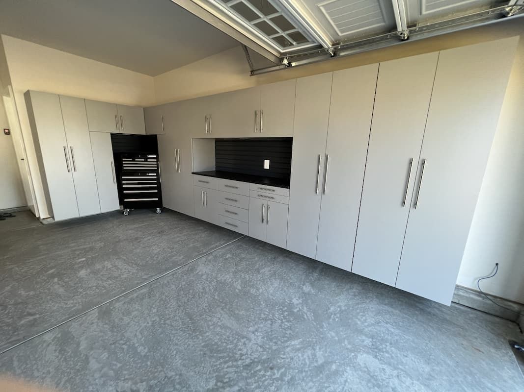Garage with light-colored cabinets along the walls, a black tool chest, and a gray concrete floor.