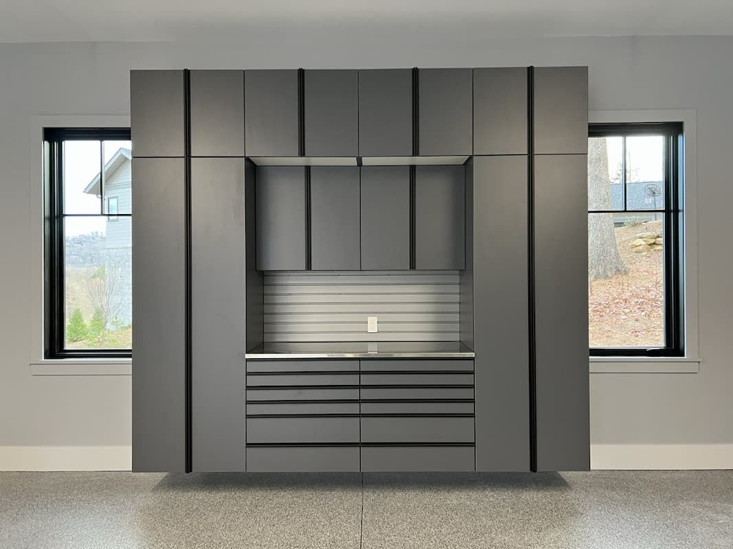 Gray built-in storage unit with cabinets and drawers, flanked by windows in an empty room.