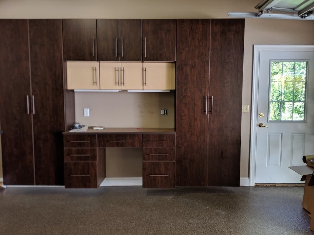 Garage with dark wood cabinets, a desk, and a light-colored door.