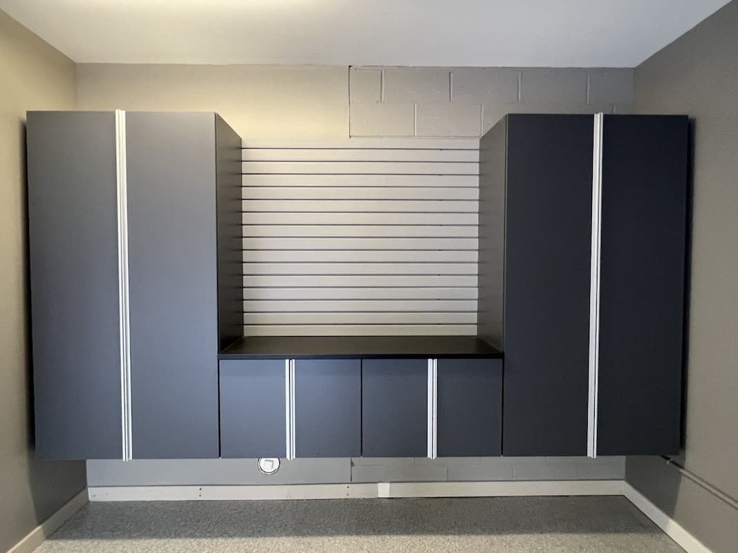 Gray garage storage cabinets and work surface mounted on a wall with slatwall background.