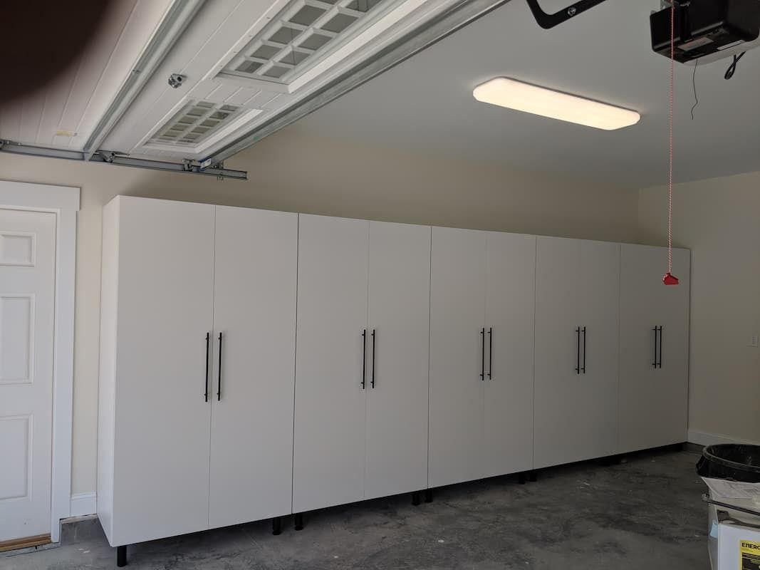 White storage cabinets line a garage wall, near a door. Garage door track and lighting are visible.