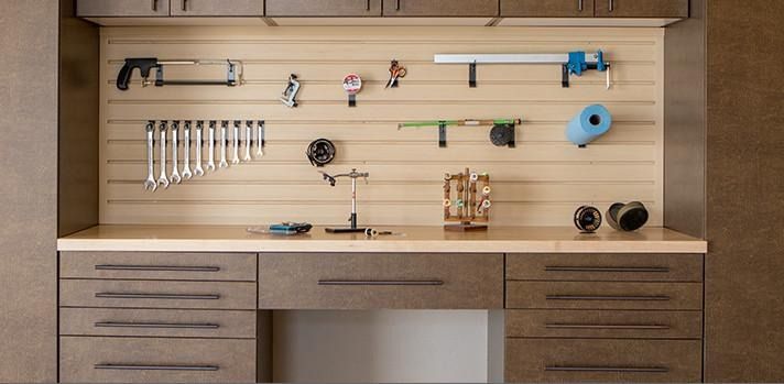 Workshop with tools organized on a slatted wall above a workbench with drawers.