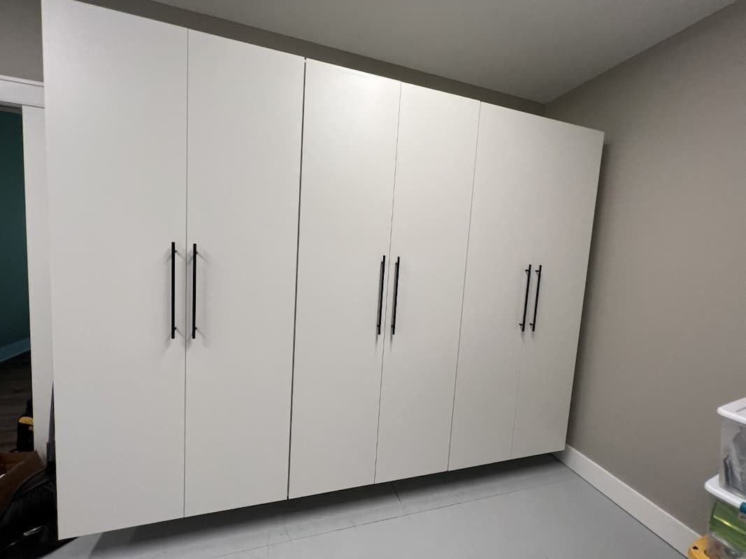 White storage cabinets with black handles in a room with light grey walls and flooring.