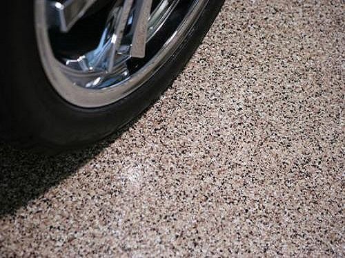 Car tire on speckled garage floor, dark tire against a multi-colored, aggregate surface.