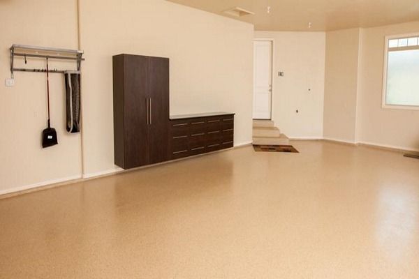 Empty, clean garage with tan flooring, white walls, and dark brown storage cabinets.