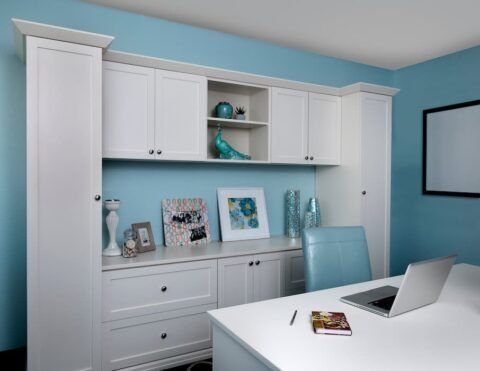White office cabinetry with desk and laptop against blue wall.