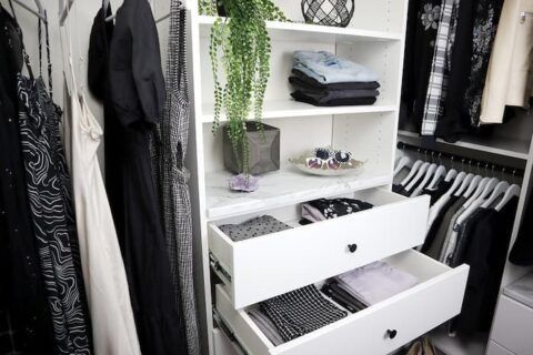 White closet with hanging clothes, shelves with folded clothes, and open drawers.