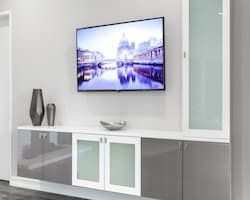 Wall-mounted TV above a modern cabinet with gray and glass doors, decorative vases, and a silver bowl.