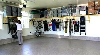 Garage with wall storage; a person reaches for items on a hanging rack. Various bins, bikes, and gear are stored.
