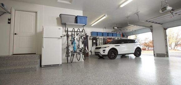 White SUV parked in an organized garage with bikes and storage. Garage door open.