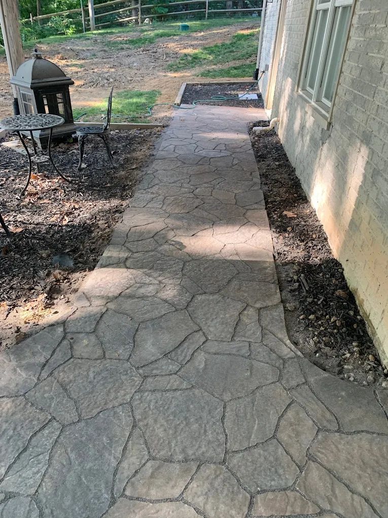 A stone walkway leading to a house with a table and chairs.