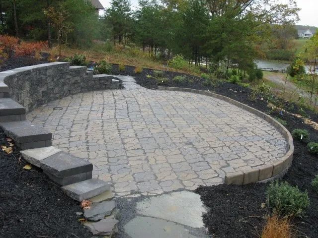 A patio with a stone wall and steps surrounded by trees.