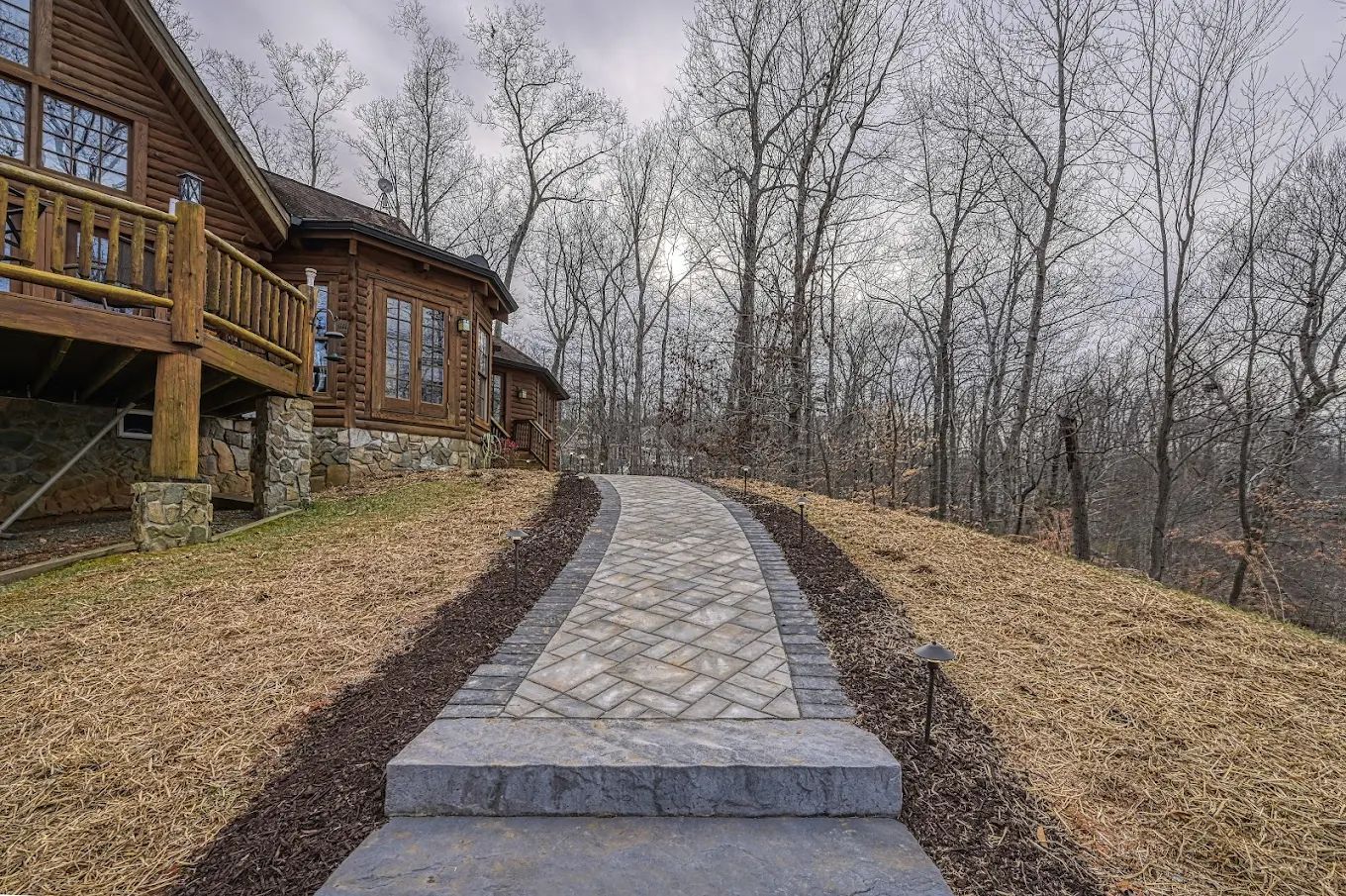 A stone walkway leading to a log cabin in the woods.