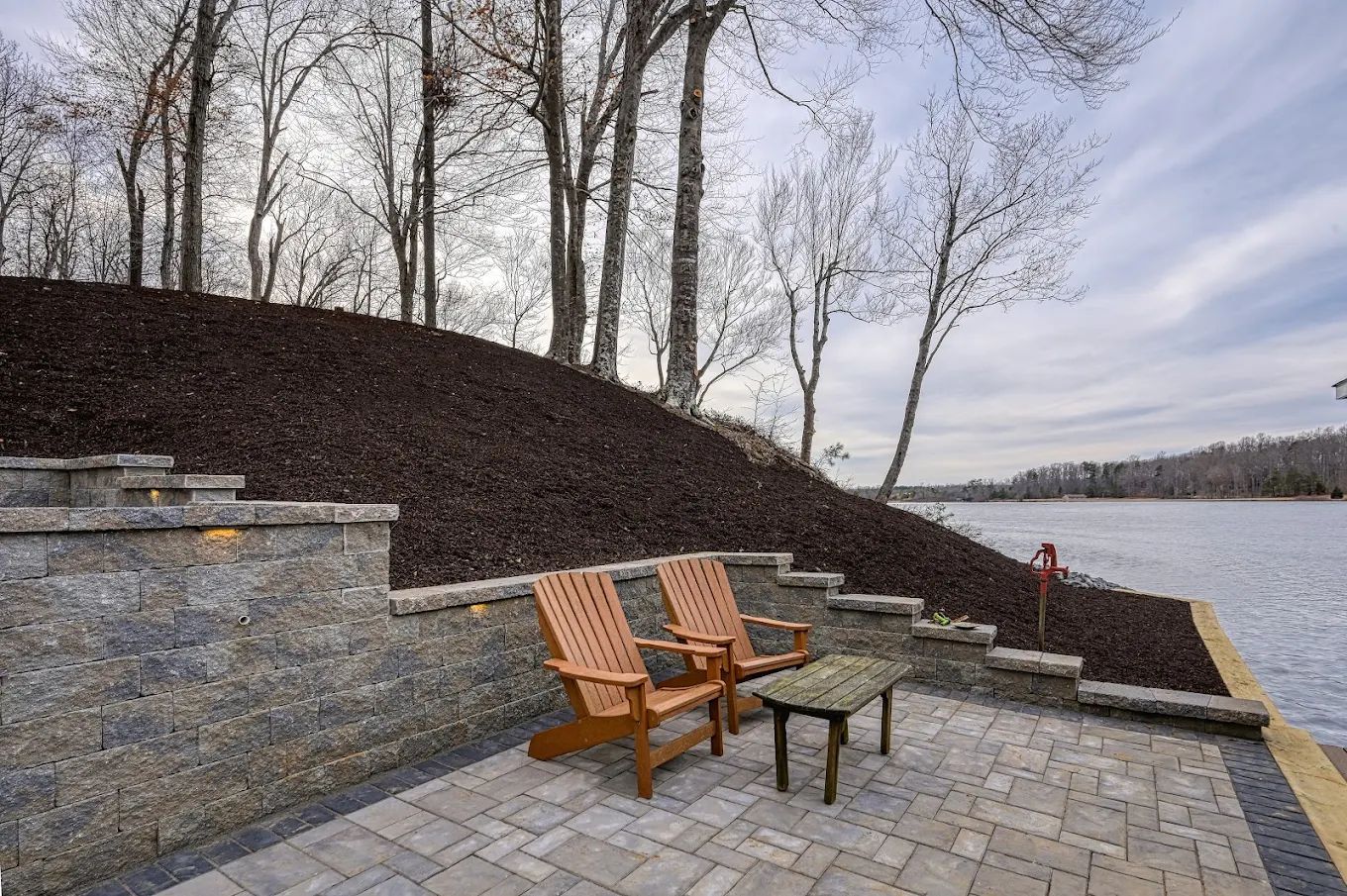 Two wooden chairs are sitting on a patio next to a lake.