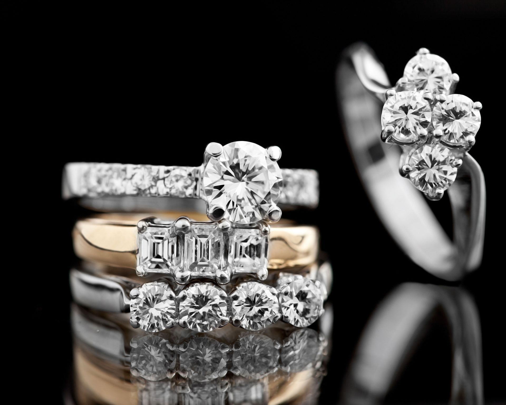 Assorted diamond rings and wedding bands on a black reflective background