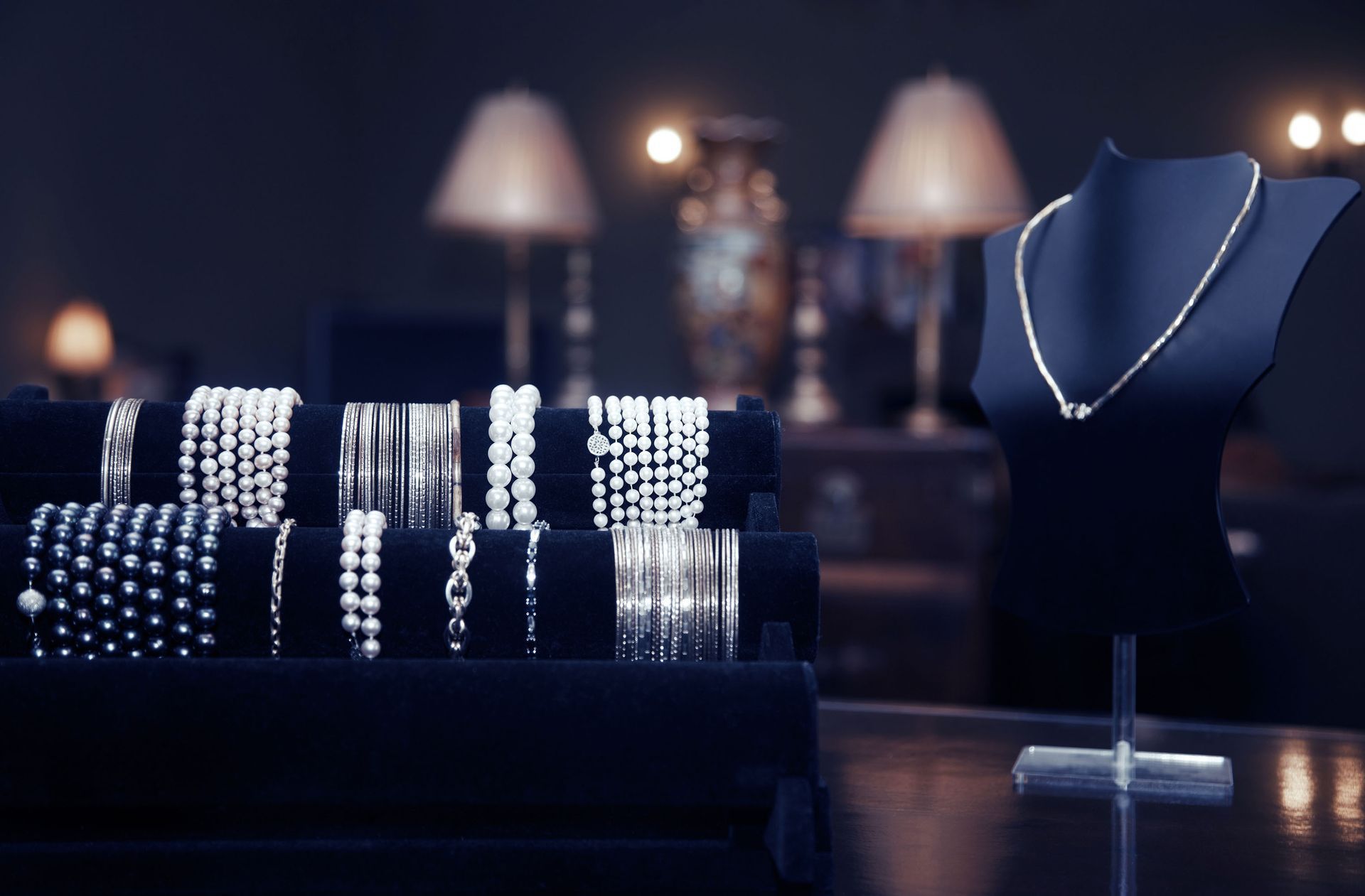 Jewelry display with pearl bracelets and necklaces on black stands in a softly lit boutique.
