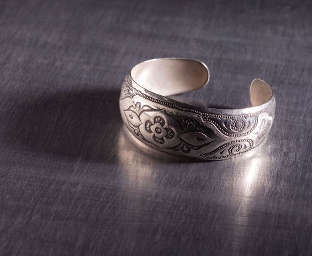 Silver engraved cuff bracelet on a dark fabric background.