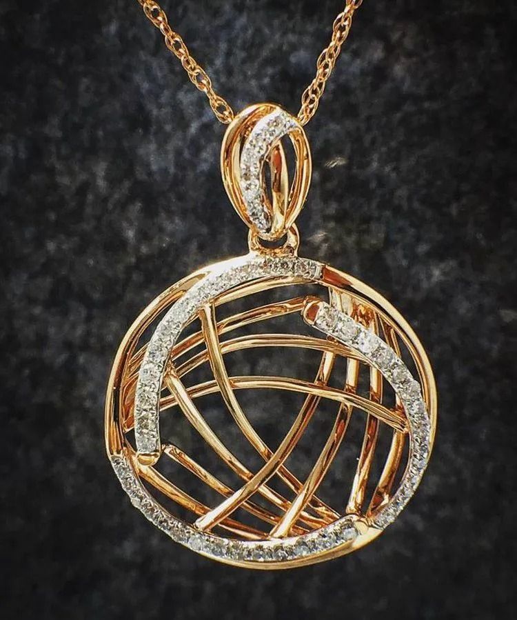 Gold and diamond circular pendant necklace with interwoven wire design on a dark background