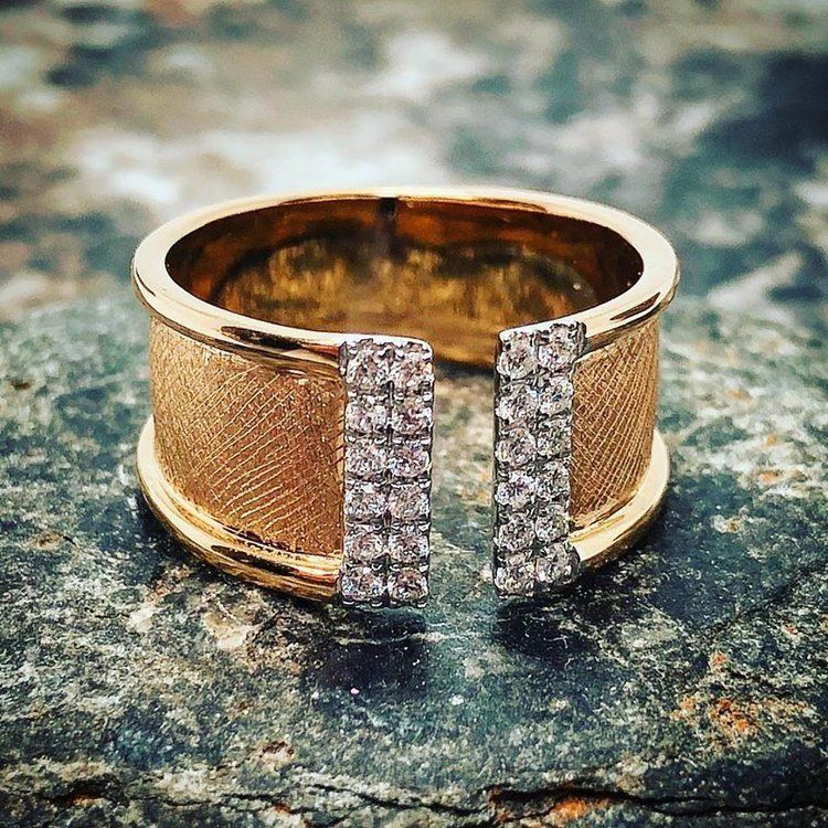 Gold cuff ring with a textured band and two vertical rows of clear stones on a stone surface