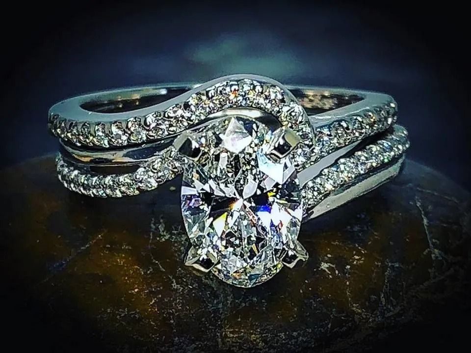 Silver diamond engagement ring with oval center stone and pavé band on a dark reflective surface