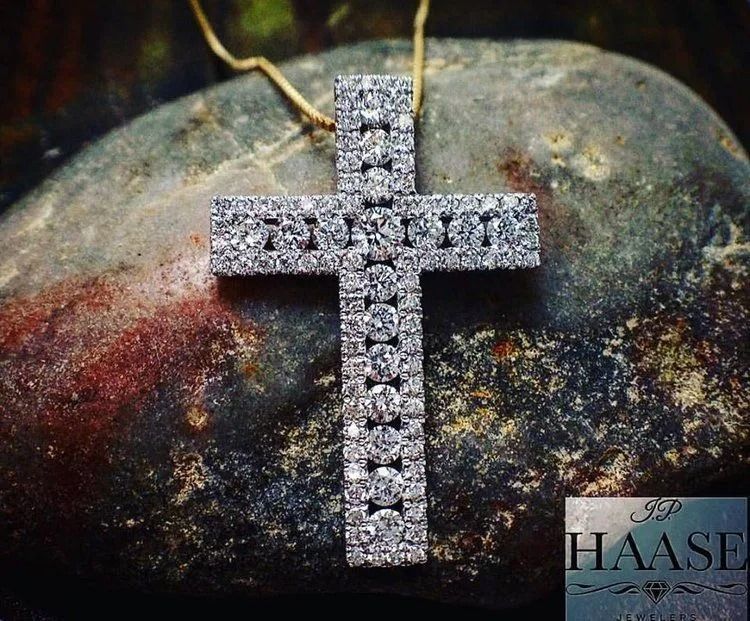 Silver cross pendant on a chain resting on a dark stone background.
