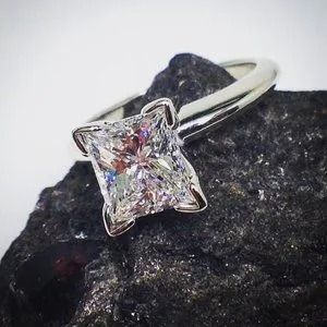 Silver ring with a square-cut clear gemstone on a dark rock background