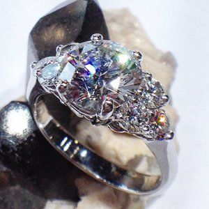 Silver ring with large clear gemstone and smaller side stones on a white background