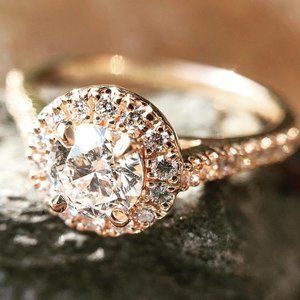 Rose gold diamond engagement ring with a halo setting on a soft brown background