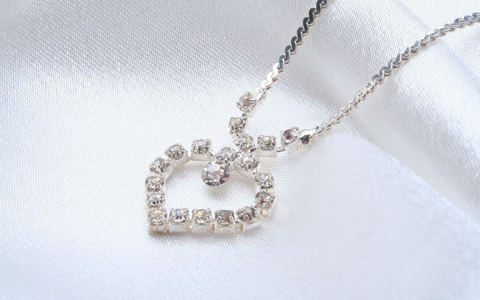 Silver necklace with a sparkling rhinestone cat-shaped pendant on a white fabric background