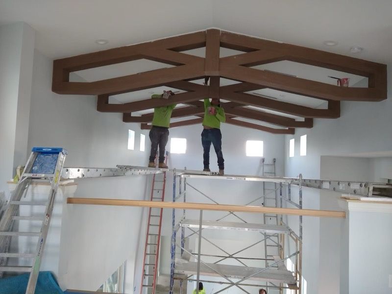 Workers installing wooden roof beams inside a white room on scaffolding.