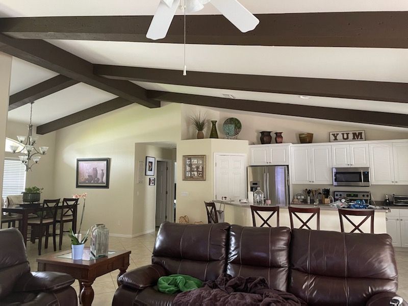 Open-concept living room and kitchen with dark wood beams, white cabinets, and leather sofa.
