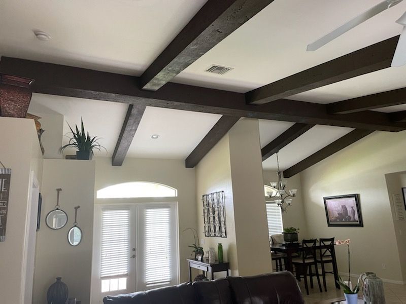 Living room with exposed dark ceiling beams, white walls, and an arched window with shutters.