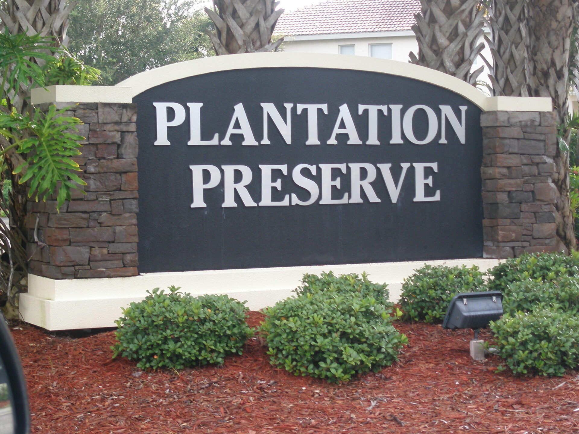 Stone entrance sign reading “Plantation Preserve” amid shrubs and palm trees