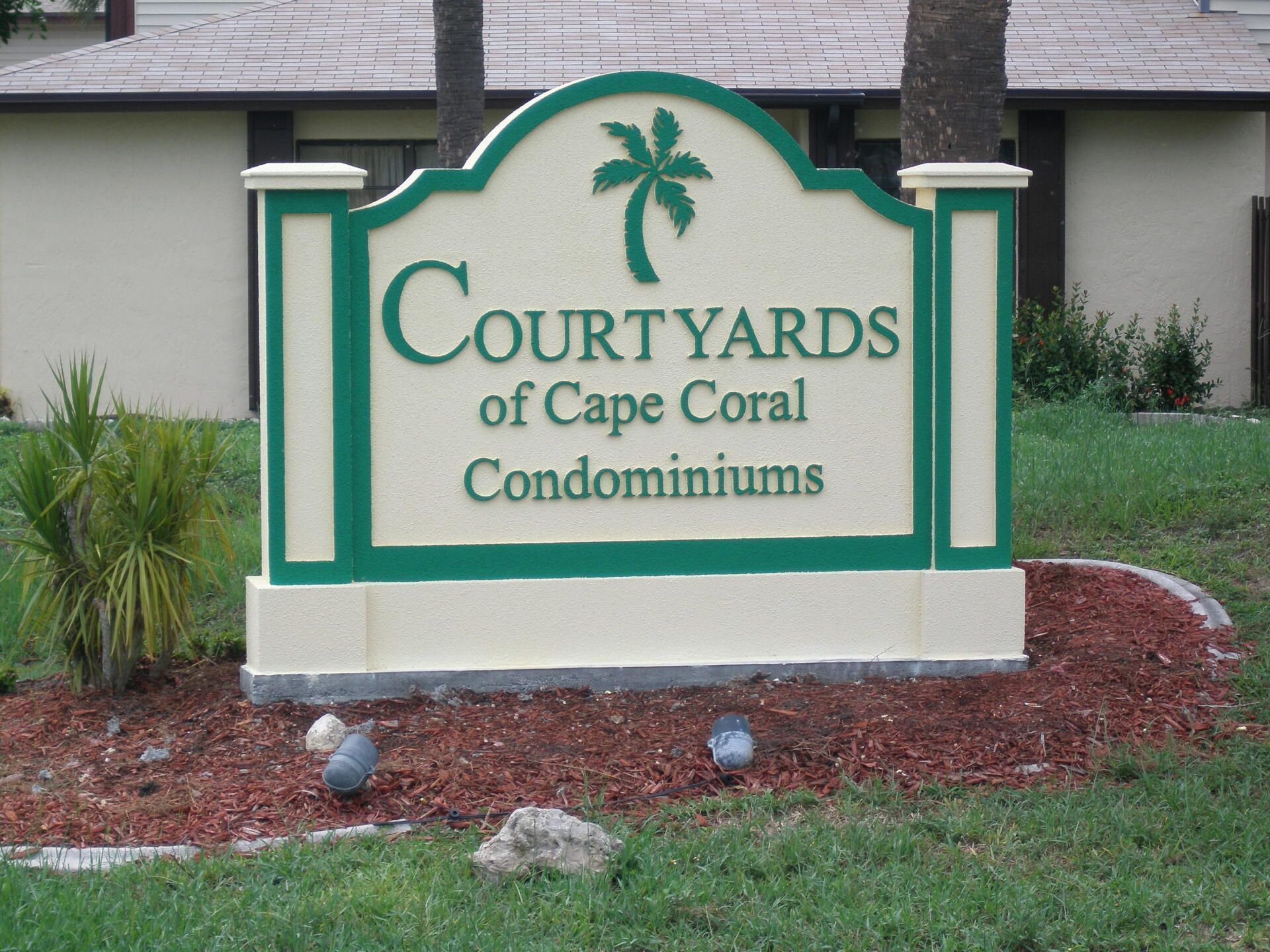 Sign for Courtyards of Cape Coral Condominiums with green trim in a landscaped area