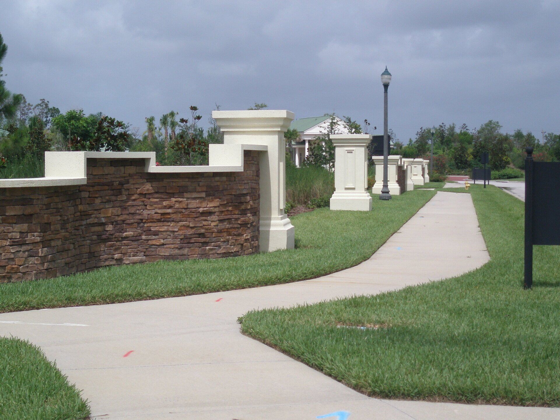 Curving concrete path beside brick and white walls in a landscaped park under cloudy sky