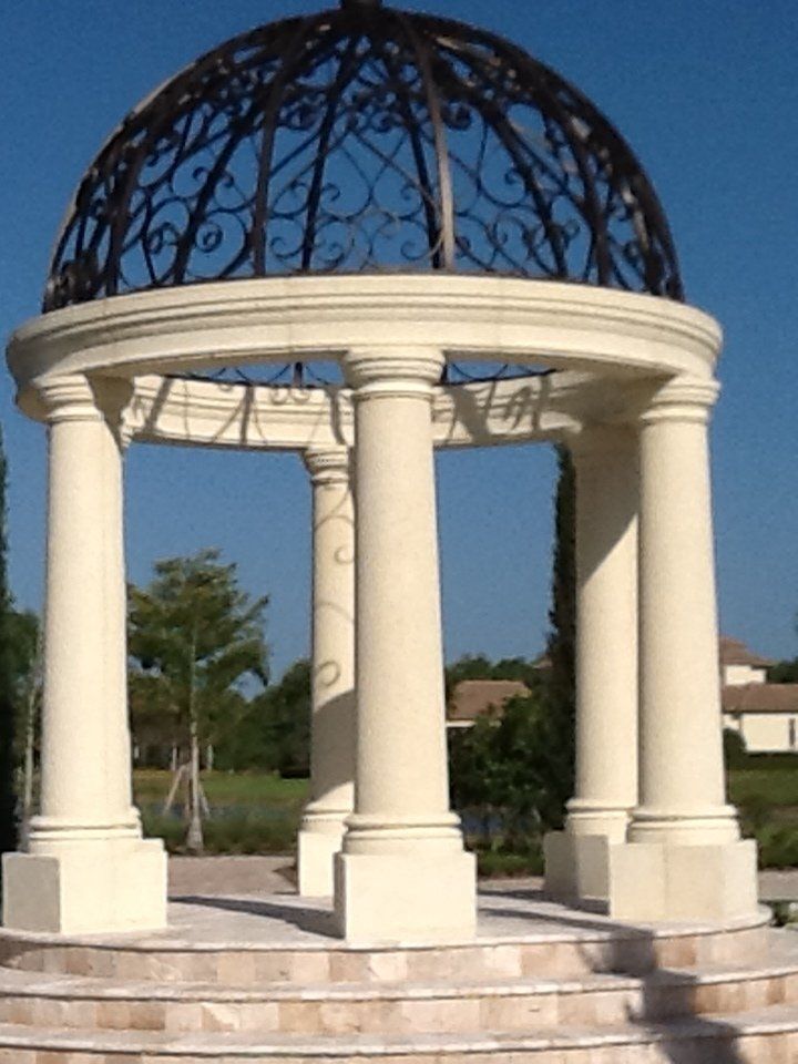 White columned gazebo with a dark blue domed roof on stone steps outdoors under a clear sky