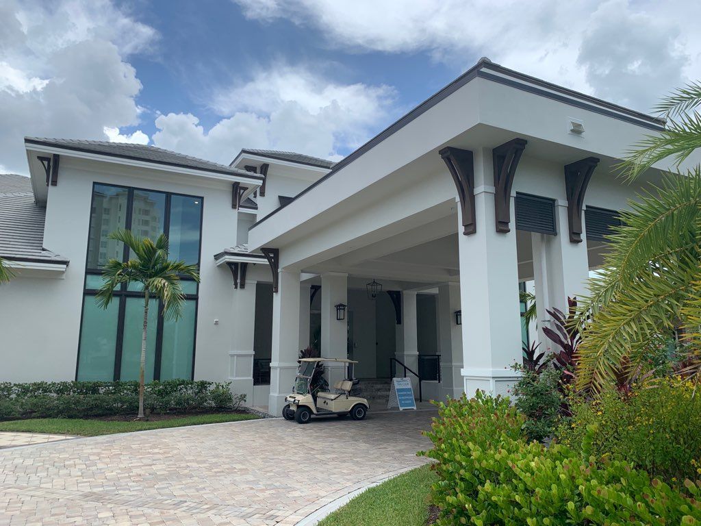 Modern white villa with tall columns, palm trees, and a golf cart in the driveway.