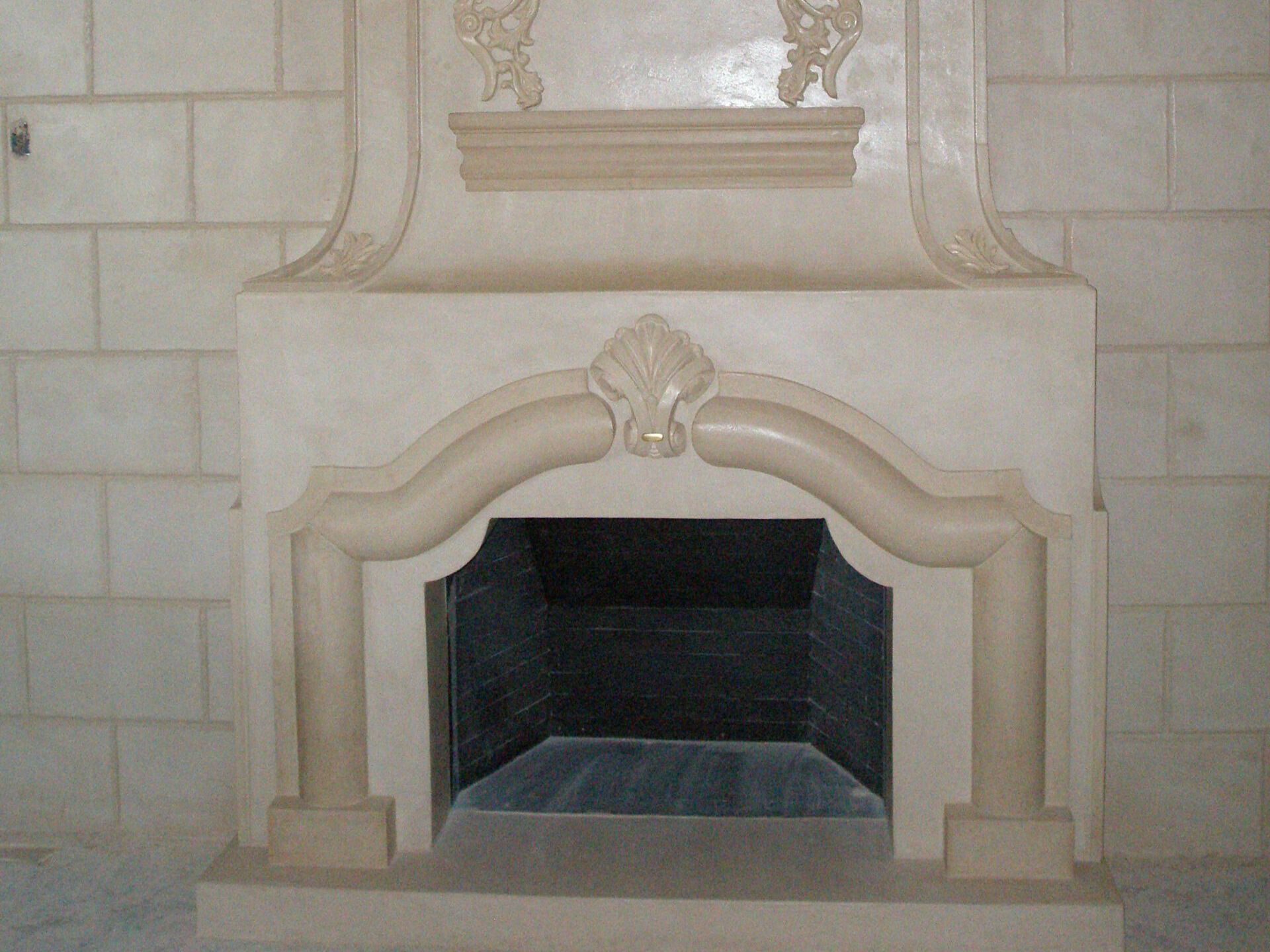 Ornate cream-colored fireplace with a dark firebox set into a tiled wall.
