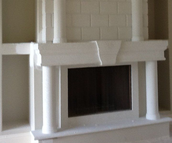 White decorative fireplace mantel with columns and a dark firebox opening in a room.