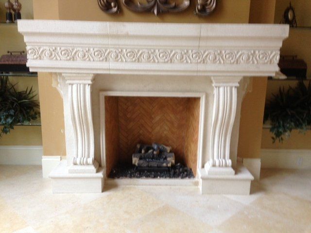 White decorative fireplace mantel with ornate columns and a small firebox in a room.