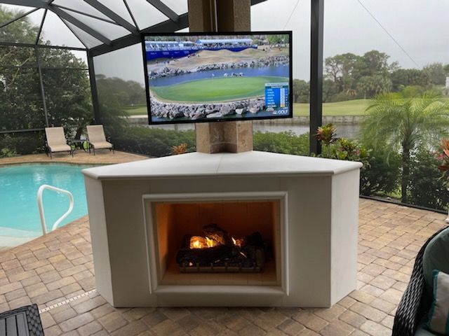 Outdoor patio with a fireplace and TV, overlooking a screened pool and garden.