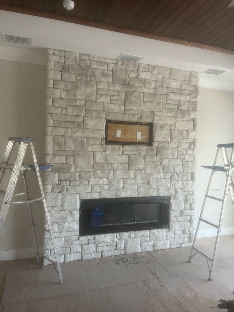 Stone fireplace wall with a mounted TV and two ladders on either side in a room under renovation.