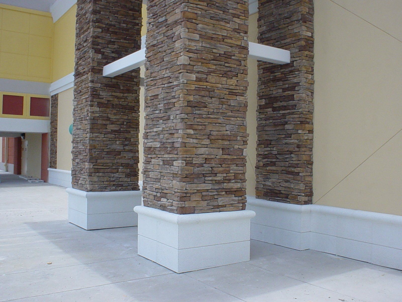 Covered walkway with stone-clad columns and white bases beside a building