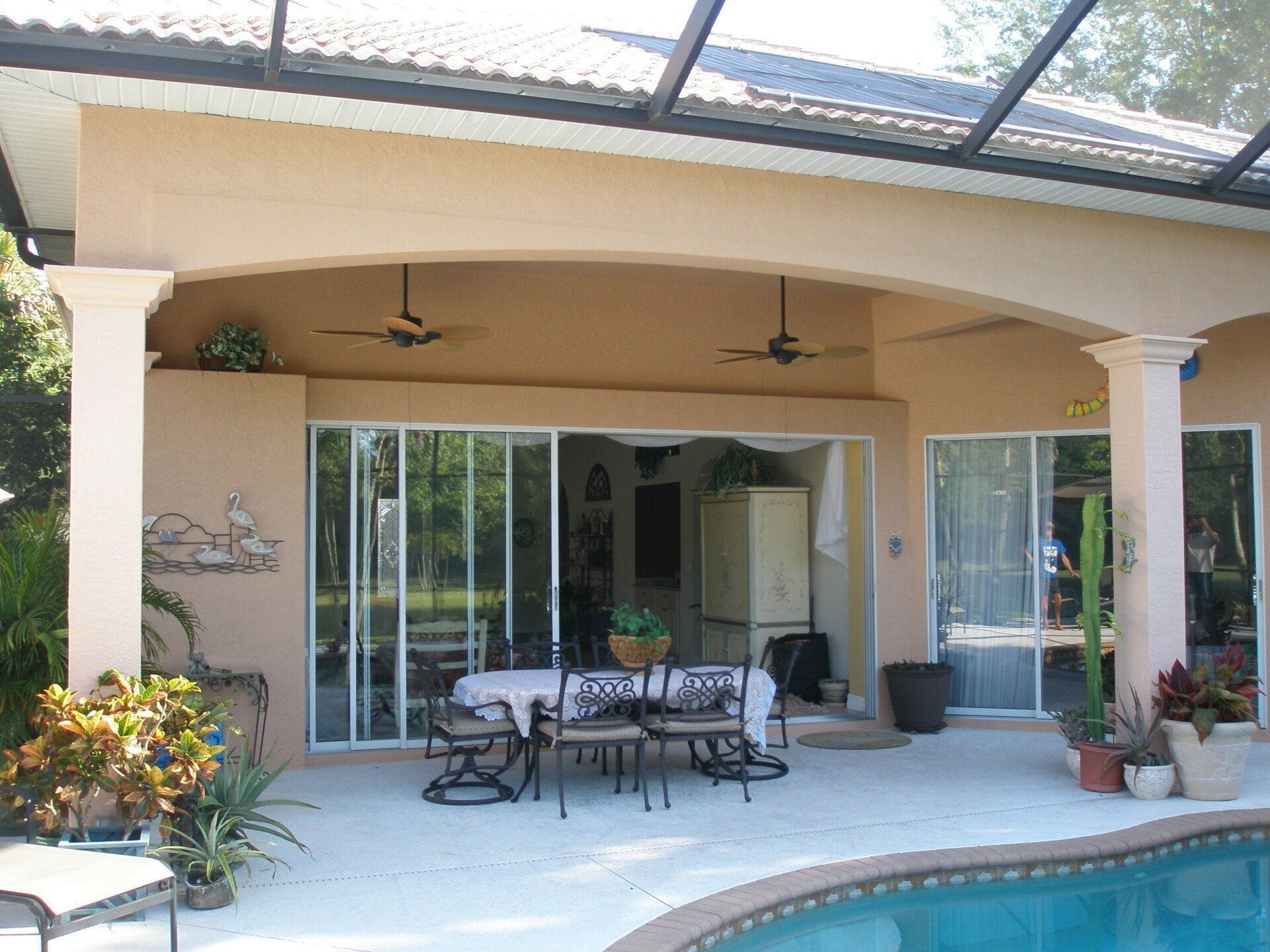 Covered patio with sliding glass doors, outdoor table and chairs, potted plants, and ceiling fans