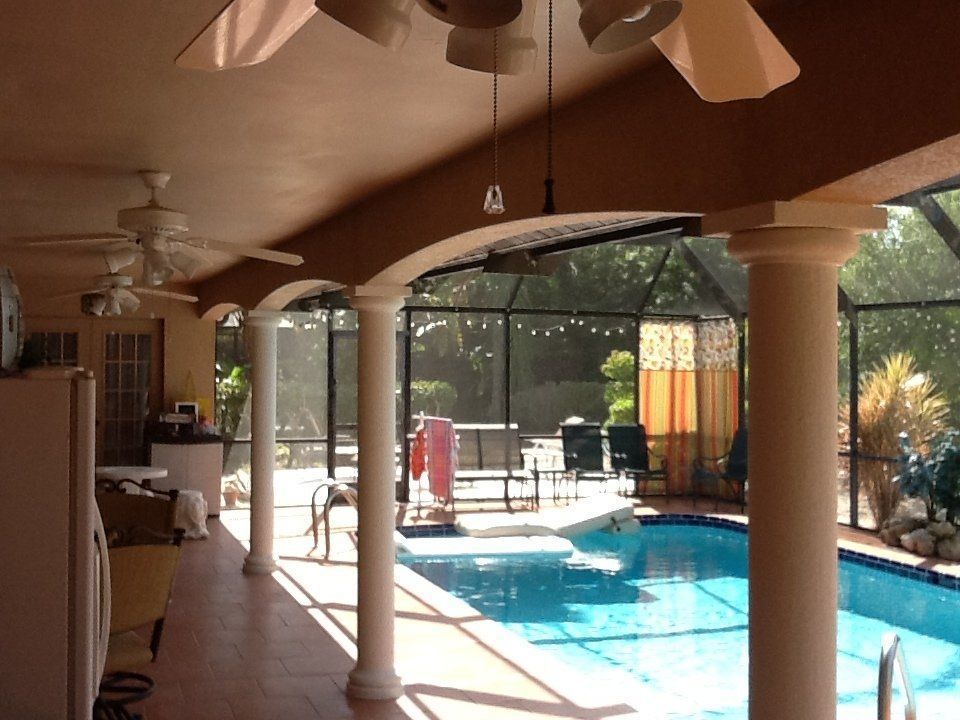 Covered patio with ceiling fans overlooking a sunny backyard pool and columns.